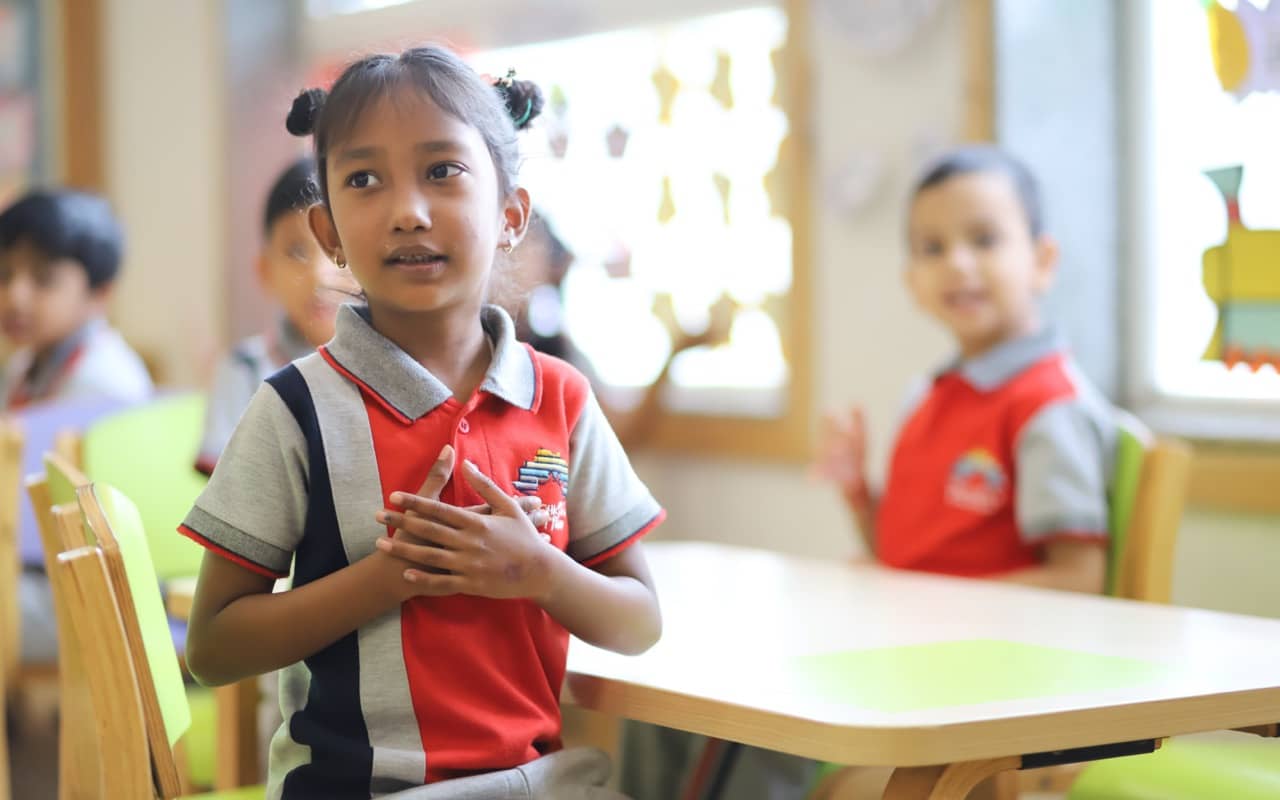 A young girl confidently explaining something to the teacher while other children watch her curiously.